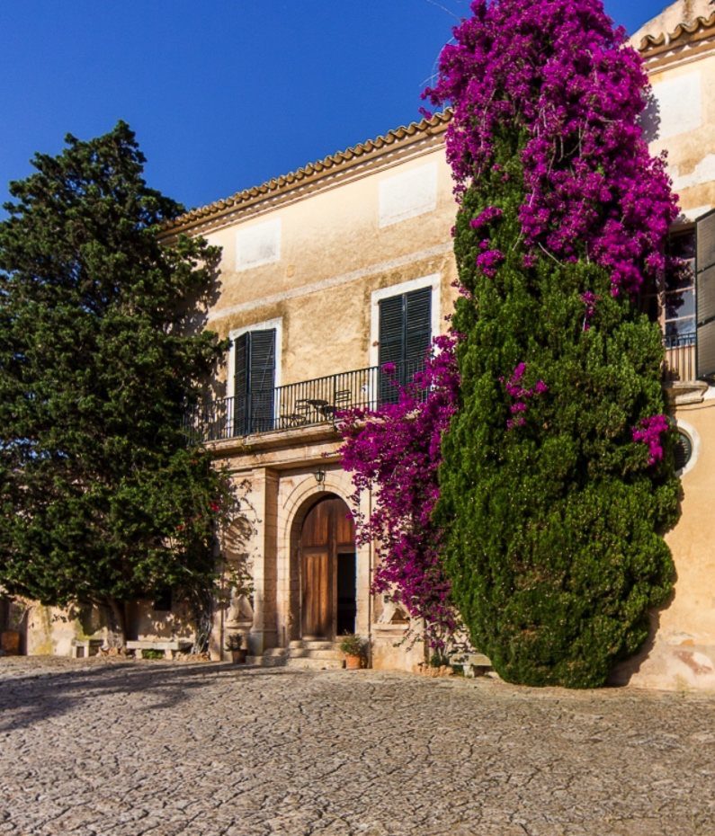 Fachada de una possessió histórica con portal de arco, ciprés y buganvilla, Mallorca